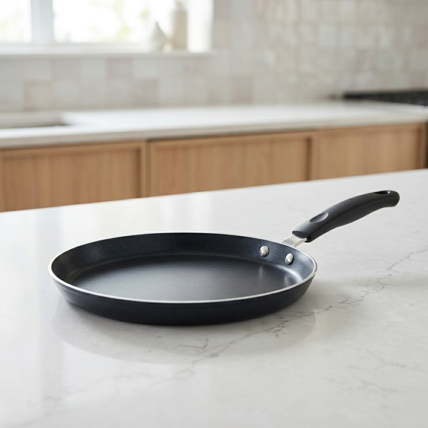 Poêle à crêpes antiadhésive noire avec manche ergonomique posée sur un plan de travail de cuisine moderne et minimaliste.