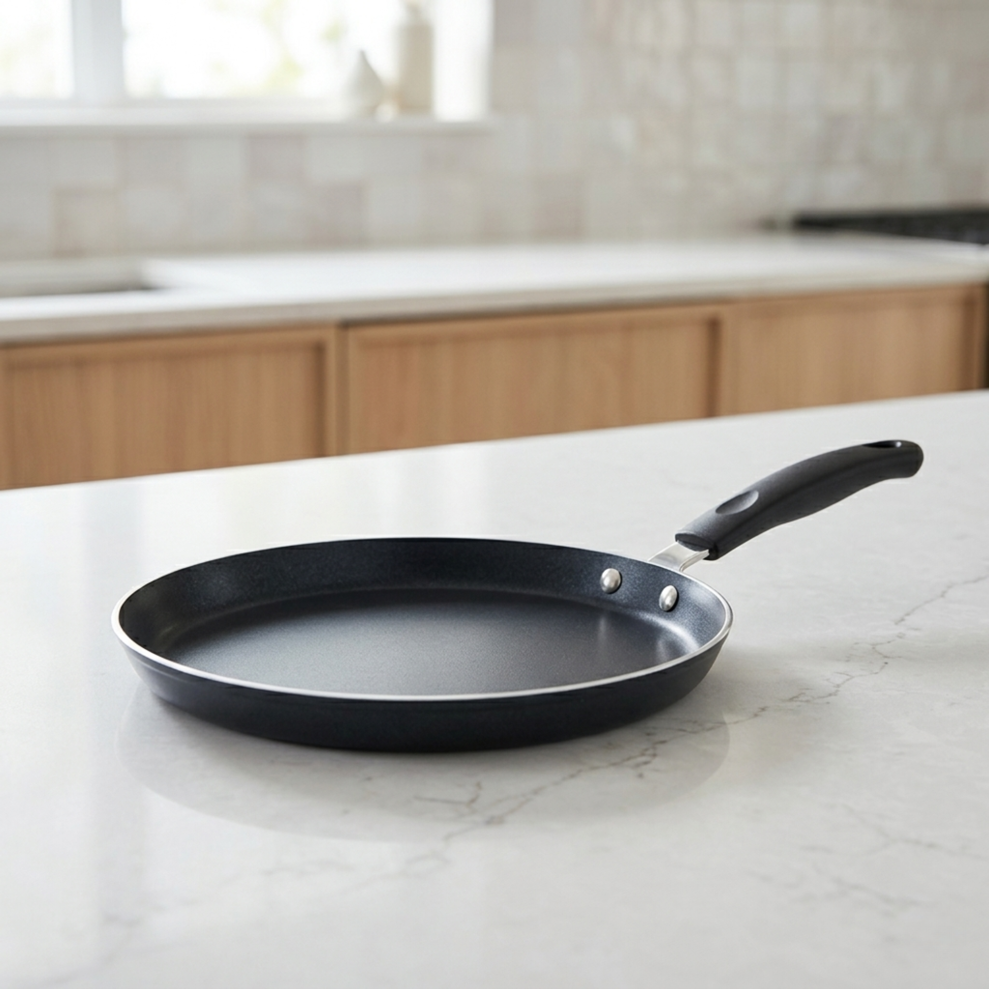 Poêle à crêpes antiadhésive noire avec manche ergonomique posée sur un plan de travail de cuisine moderne et minimaliste.